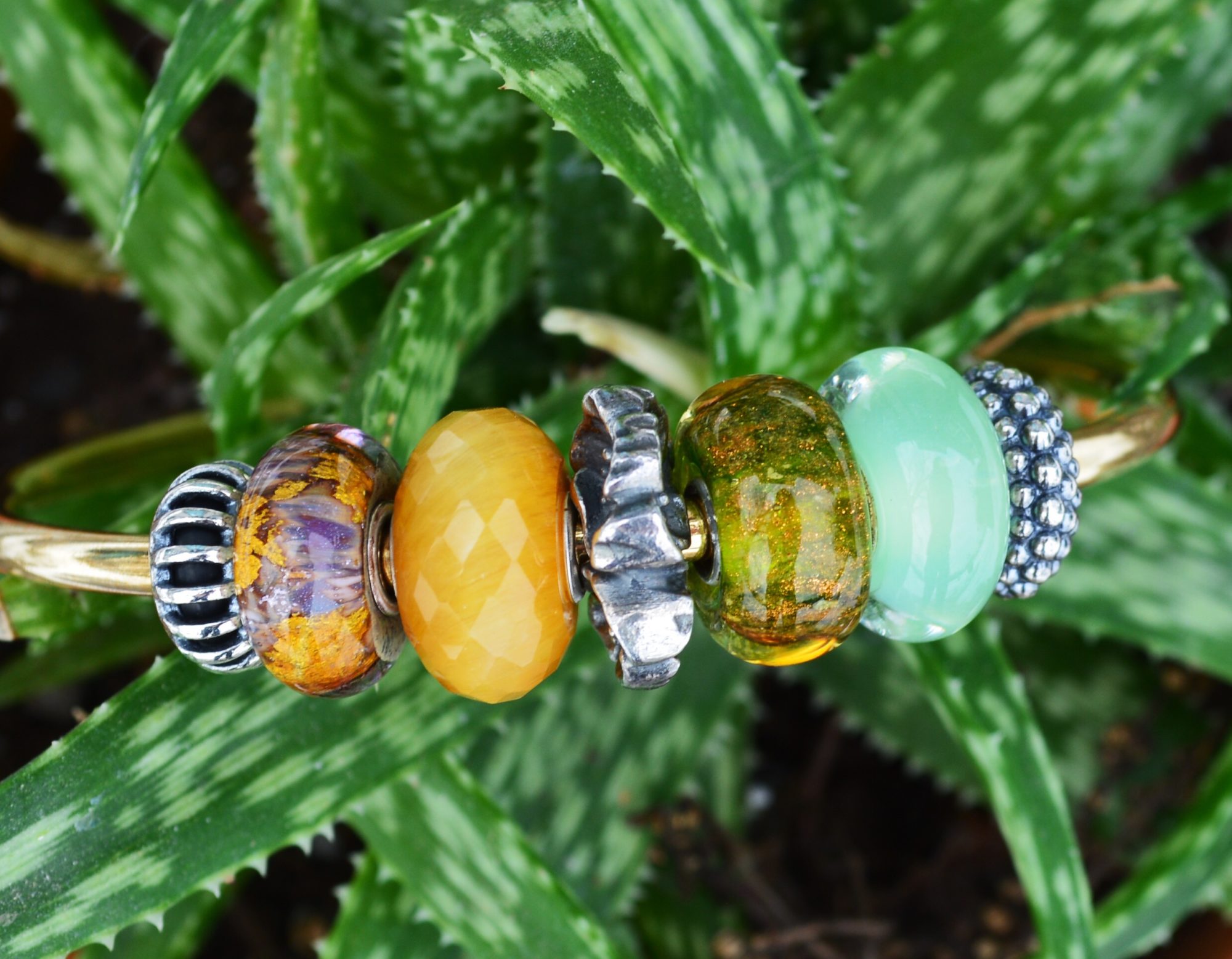 Bright beads pop on a deep green backdrop, Trollbeads- inspired by nature